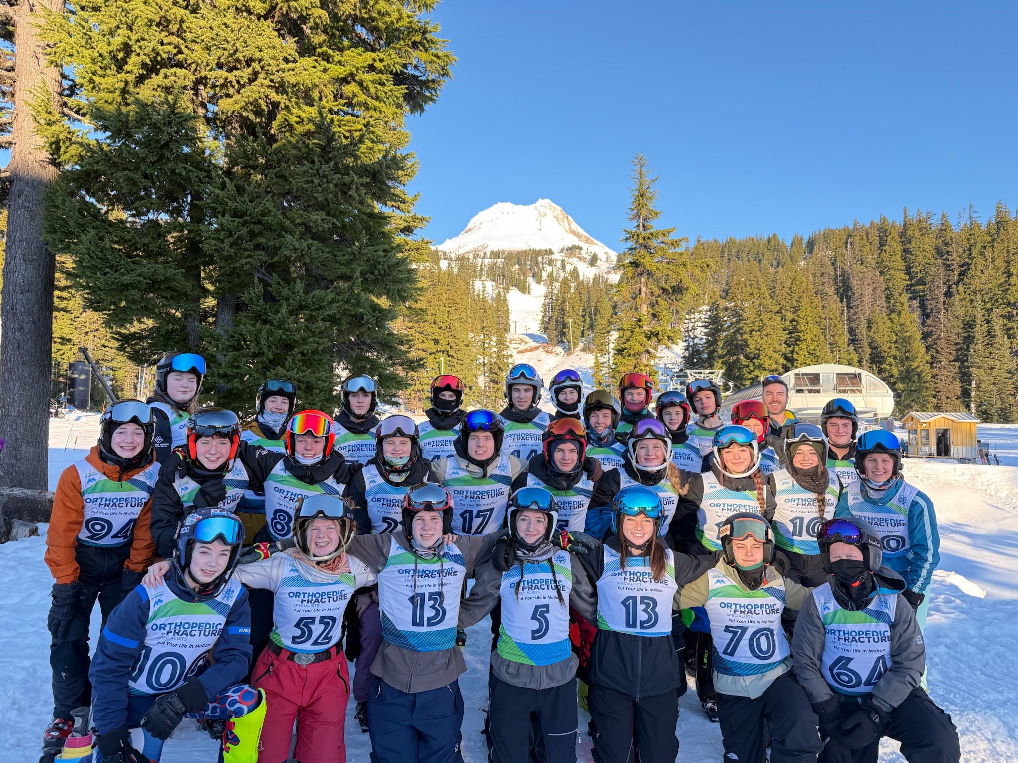 Southwest Mountain racers and a coach together in race bibs on the snow, with the mountain behind them